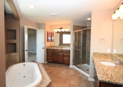 Bathroom with whirlpool tub, 2 vanities & clear glass tile shower.