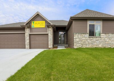 Ranch home with earth tone stone accents and yellow banner above the 3 car garage door.