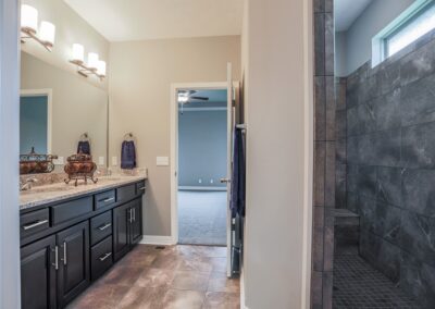 Bathroom with walk in shower, two sinks, quartz countertops, and black birch cabinets.