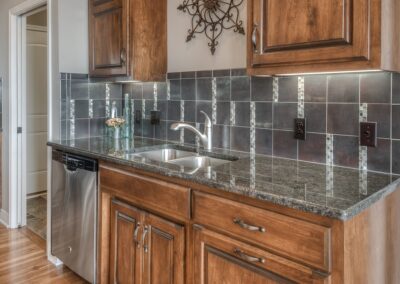 Stainless kitchen sink with dark tile and granite countertop.