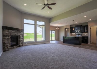 Family room with tall ceilings, stone fireplace and black kitchen cabinetry.