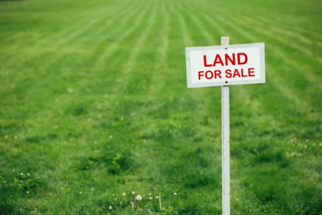 Vacant lot for sale with red and white sign. Talk to a home builder before you buy a lot.