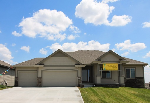 This ranch home front elevation by aurora homes in omaha, ne has a 3 car garage and covered porch. Lovely blue sky and green grass. Who could ask for more?
