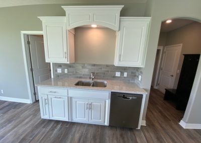 Kitchen sink with valance and overhead lighting. Rear foyer in background.