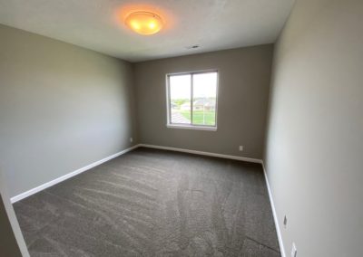 Unfurnished bedroom with large window and grey carpet.