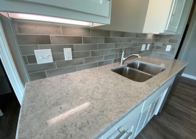 Stainless steel kitchen sink with fog quartz countertop, tile backsplash and under-cabinet lighting
