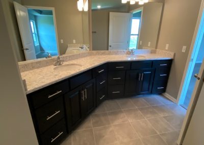 Primary bathroom vanity with dual sinks, large mirrors, and stained birch cabinets.