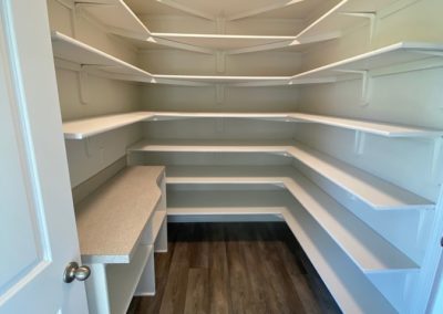 Huge walk-in pantry with countertop and wood shelving by Aurora Homes.