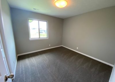 Bedroom with bright window and grey carpet.