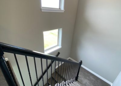 Staircase with large windows and modern black handrail by aurorahomesomaha.com
