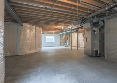 Unfinished basement with large window and HVAC ductwork.