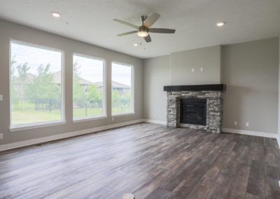 Unfurnished family room with large windows, gas fireplace and wood vinyl flooring.