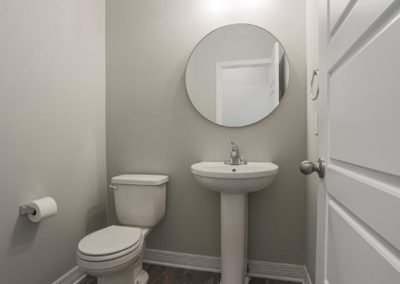 Powder bathroom with pedestal sink and round mirror.