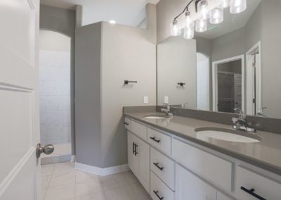 Bathroom with white dual sink vanity, grey quartz top, and walk-in shower by Aurora Homes Omaha.