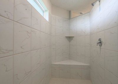 Walk in shower with angled bench seat and shelf. Natural daylight pouring through privacy window.