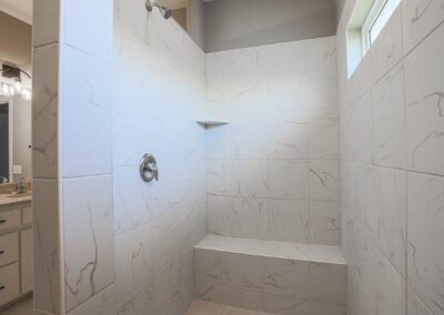 Walk-in Shower with bench seat, rain-glass window and white tile.